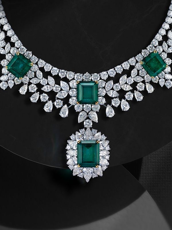 A necklace with a square green-toned pendant and coordinating pieces shown on a dark display.