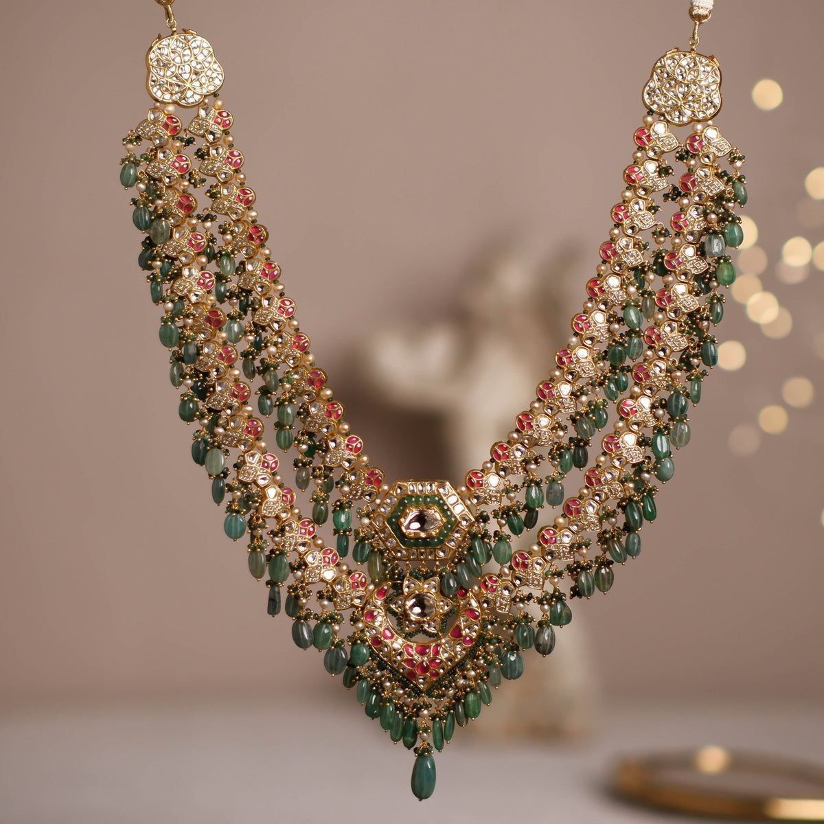 A broad layered necklace with green and rose-toned details and a center drop.
