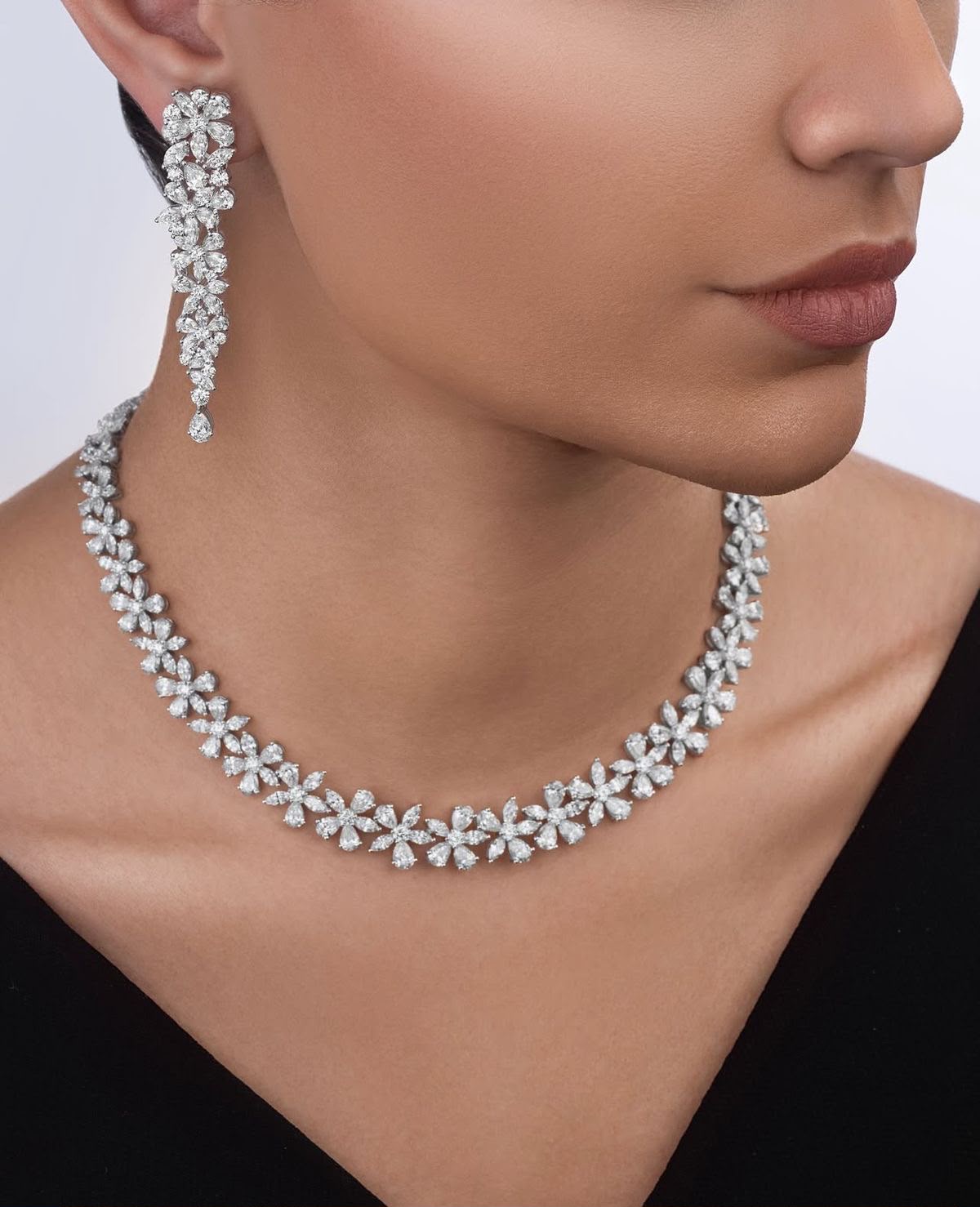 A curved necklace with floral details and matching drop earrings, shown worn.