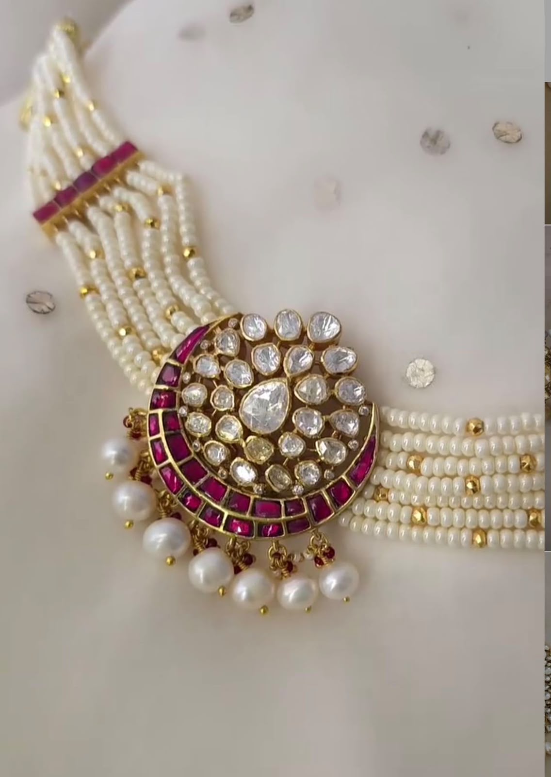 Several pale strands meet at a large round framed pendant with hanging drops.