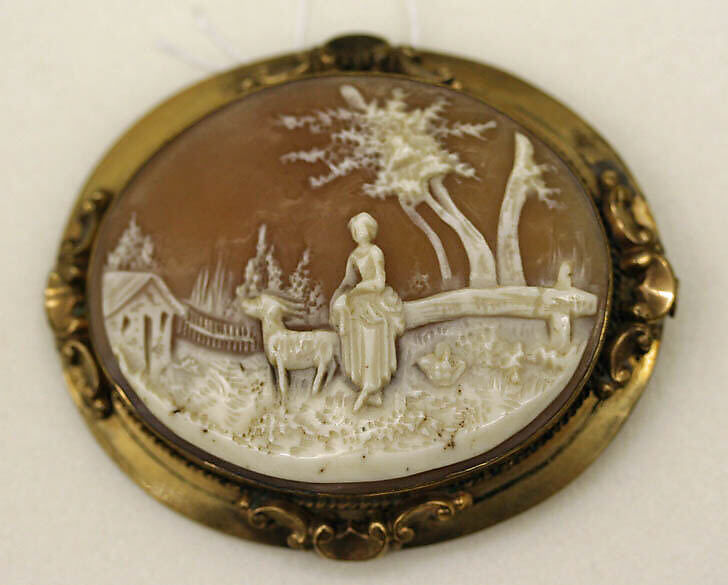 An oval cameo depicting a pastoral scene with a figure, an animal and trees. The pale relief stands against a warm background within an ornamental gold frame.