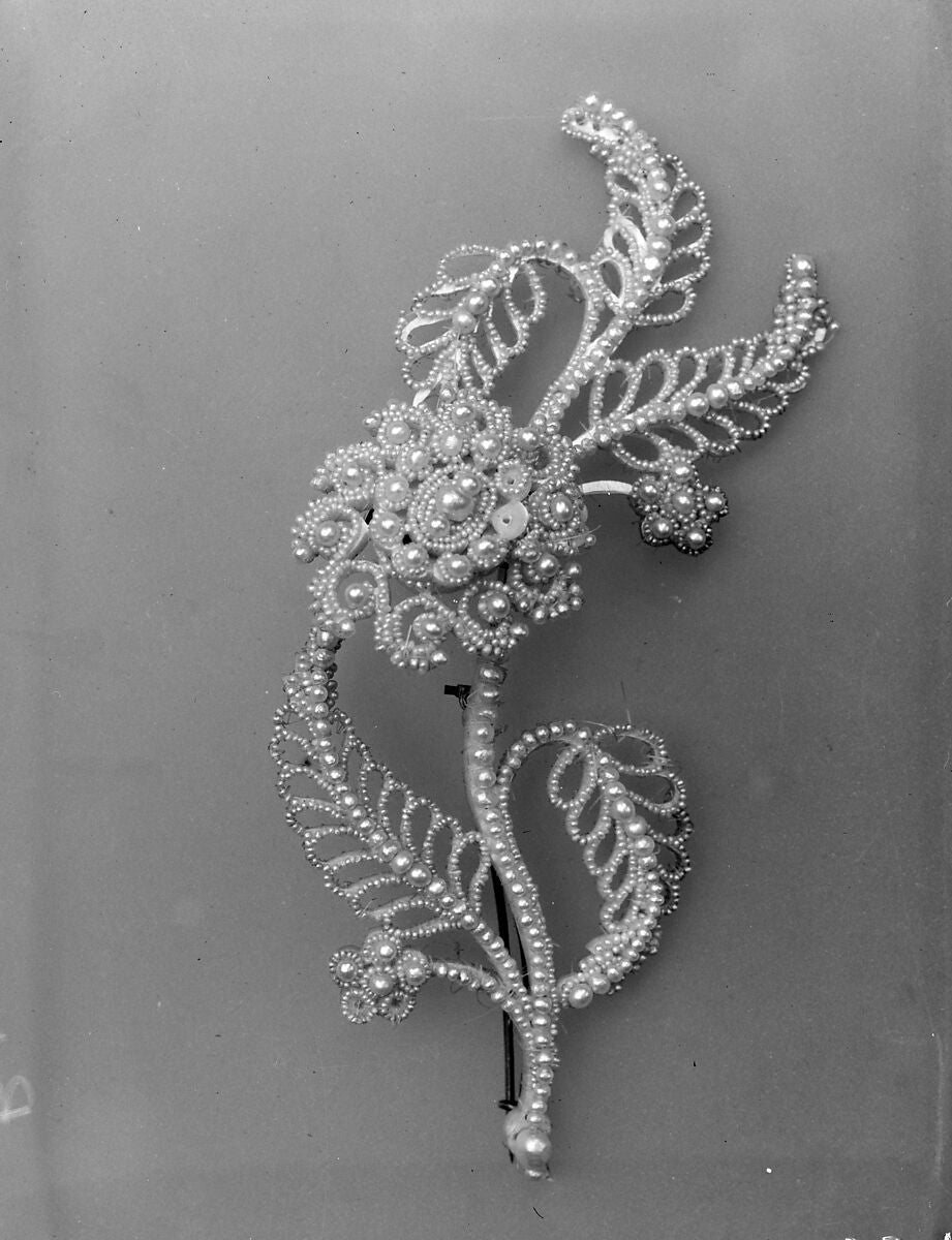 A flowing botanical spray with curling openwork leaves and small pearl accents. The elongated form brings together floral clusters and delicate fern-like curves.