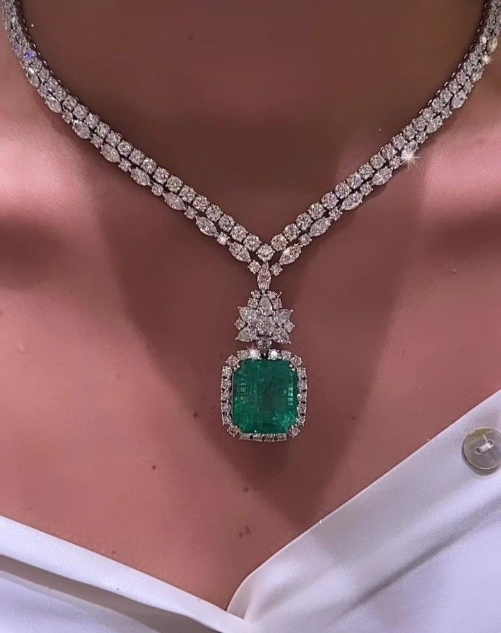 A delicate necklace with a square green-toned pendant shown against a pink background.