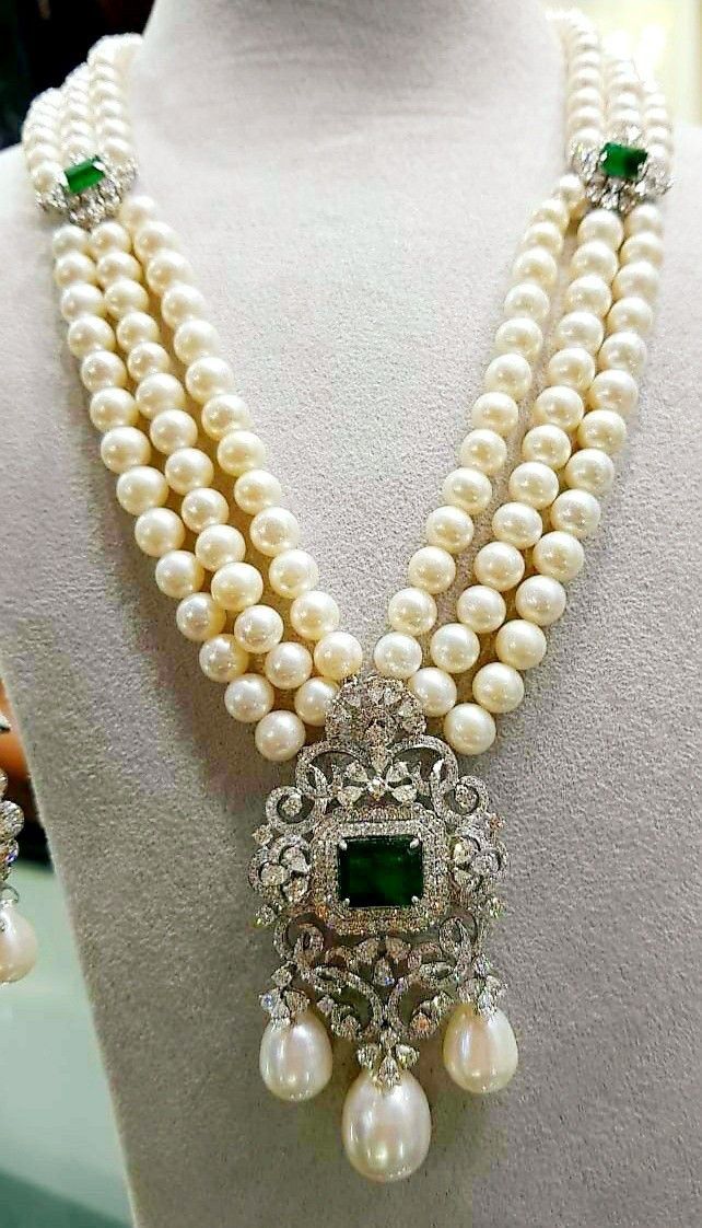 Several pale bead strands meet at a green-toned pendant with hanging drops.