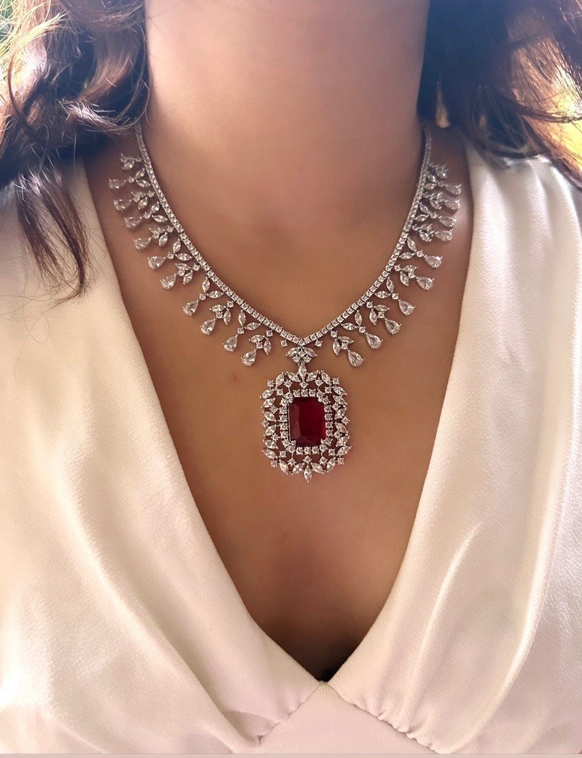 A necklace with a red-toned square pendant and pale drop accents.