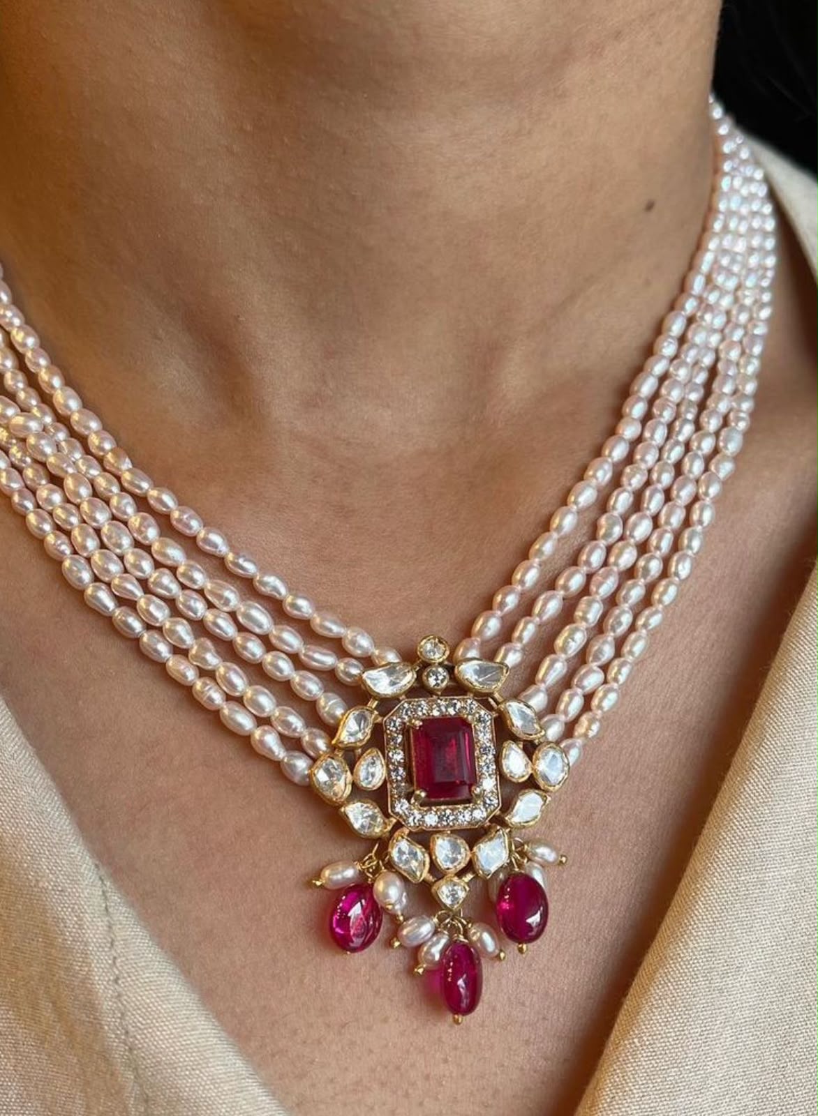 Several pale strands meet at a red-toned center pendant with hanging drops.
