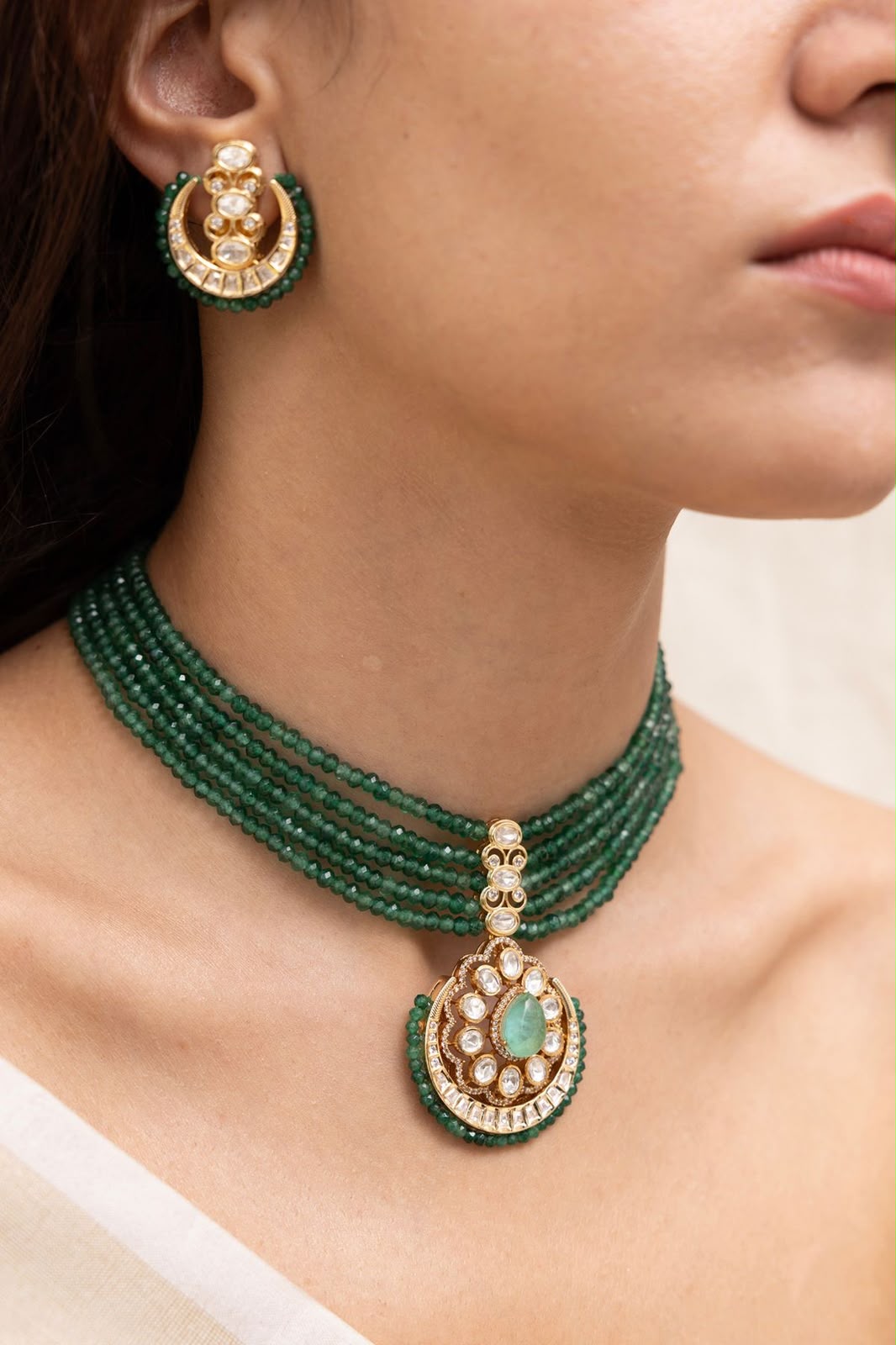 A multirow green-toned necklace with a matching earring shown beside it.