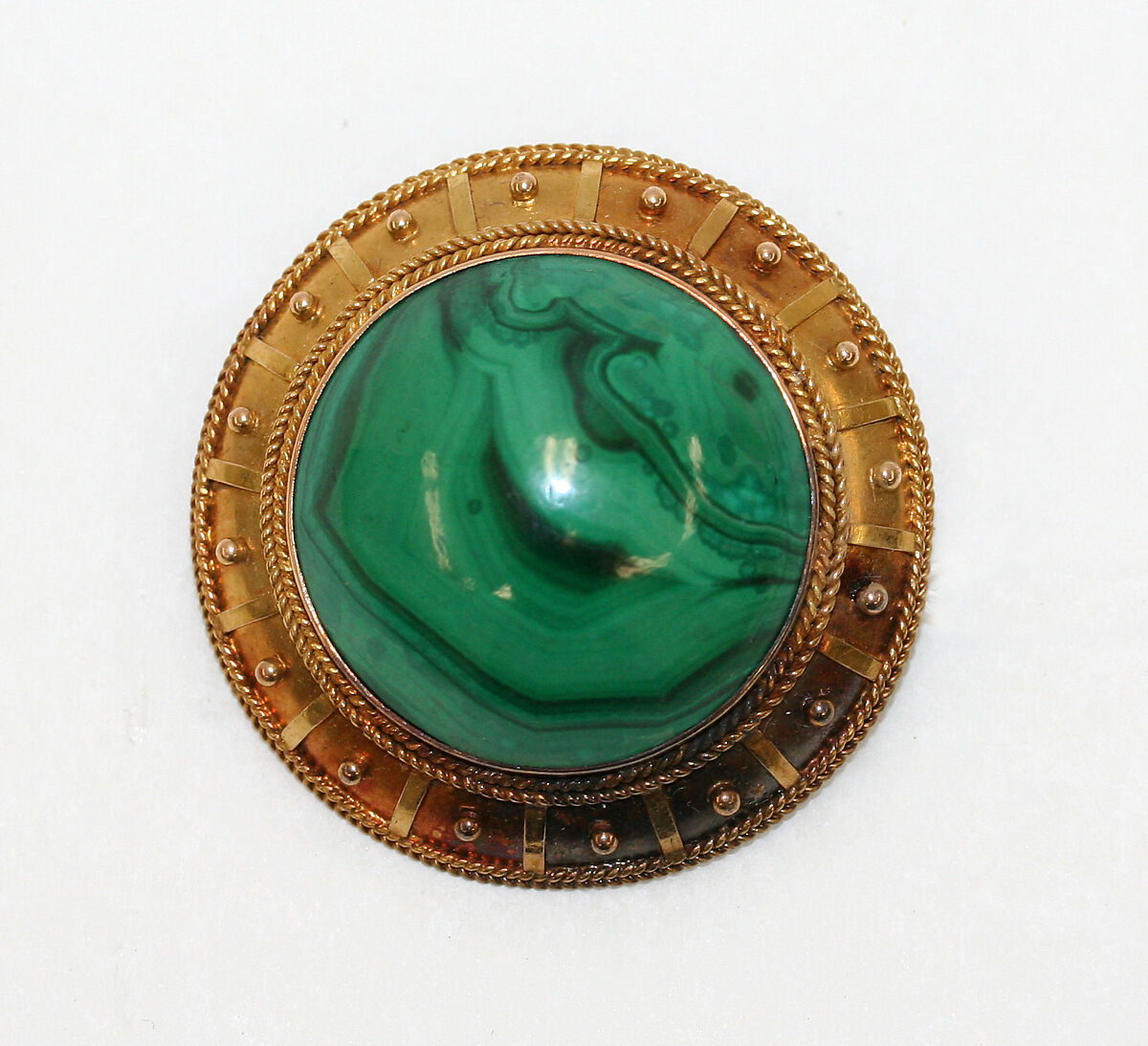 A round malachite centre with rich green banding, framed by a gold surround with braided borders and small raised details. A balanced medallion silhouette with a vintage character.